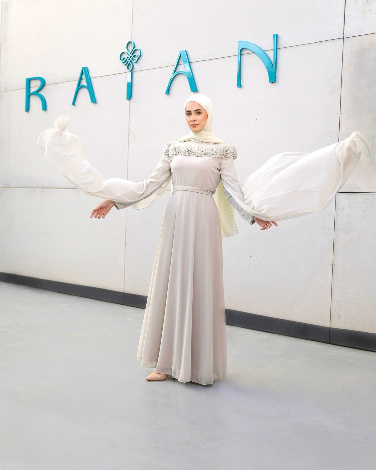 Elowen Dress in greige, with an embellished upper bodice, long cape-style sleeve panels and a flowing skirt.