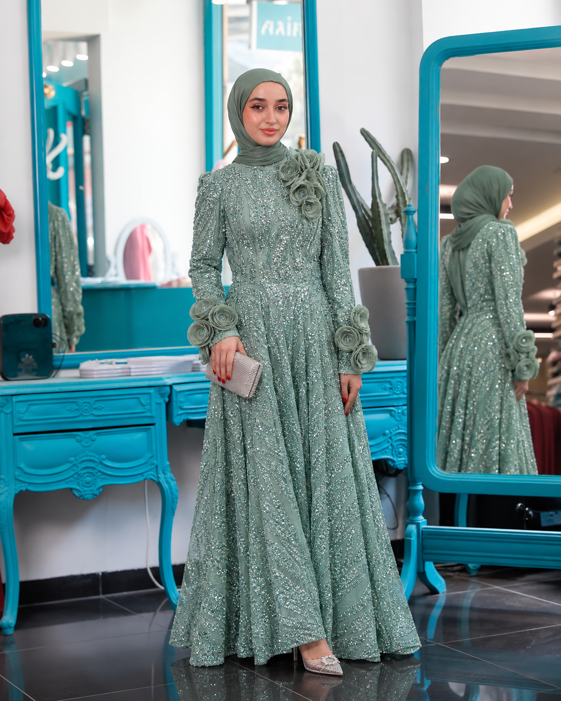 Blooming Crystal Gown shown in green, with sparkling decoration, long sleeves and rosettes at the shoulder and wrists.