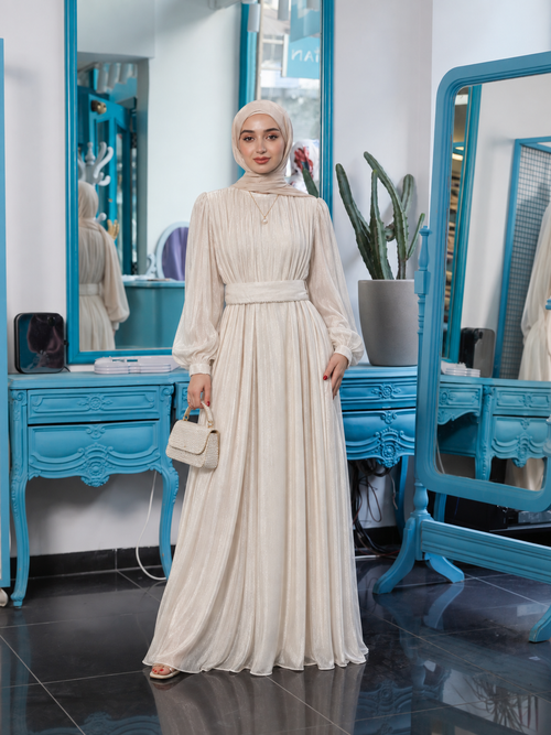 Adeline Pleated Gown in beige, with long gathered sleeves, a wide waistband and a full pleated skirt.