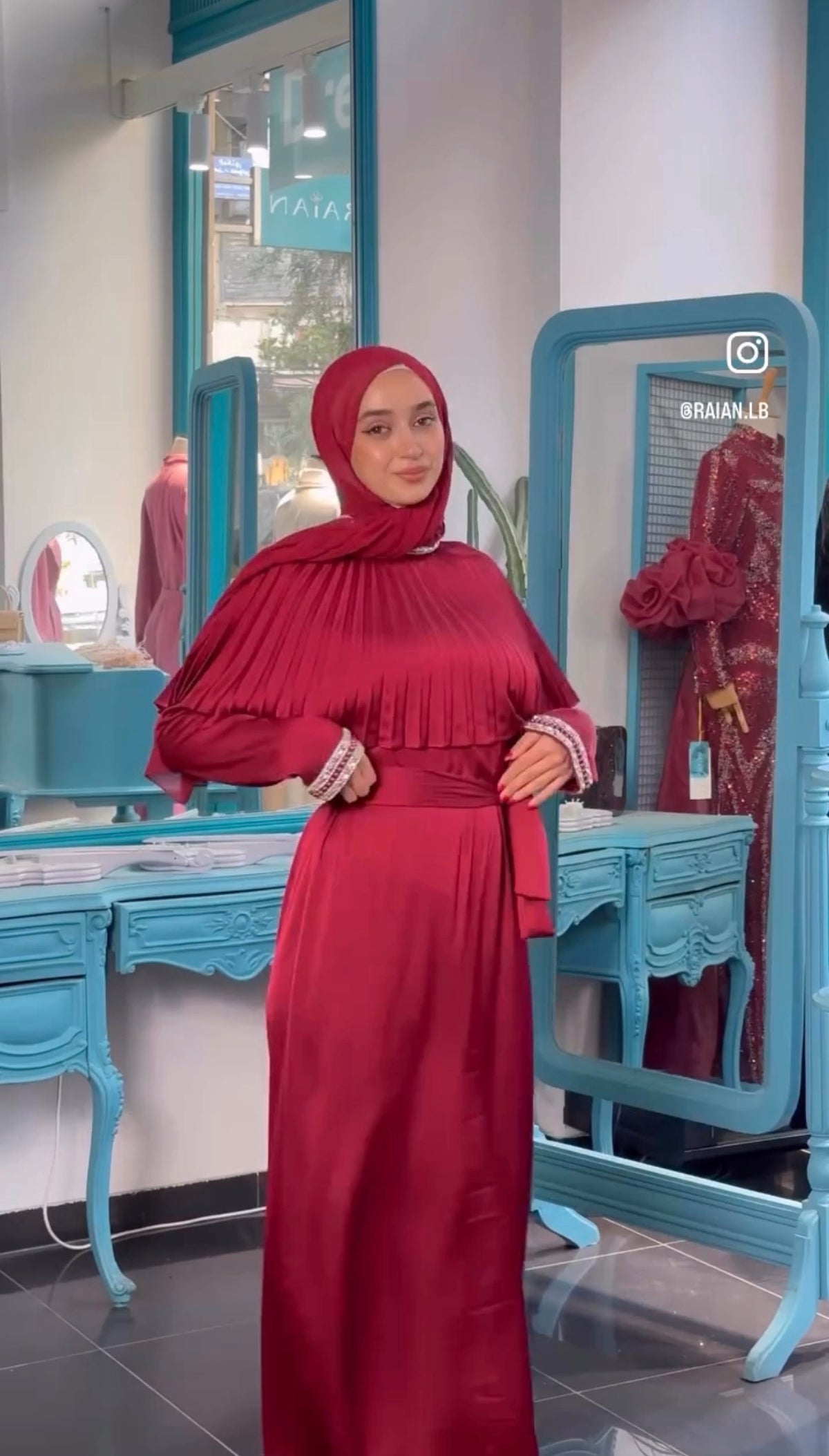 Product photo showing red Valeria Cape Dress with pleated shoulder draping, a waist tie and decorative cuffs