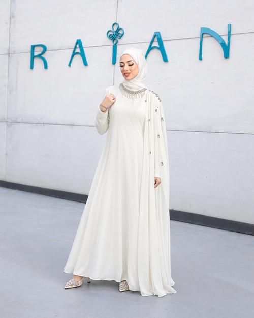 Aureline Dress in white, with an embellished high neckline, long sleeves and a decorated cape-style shoulder drape.