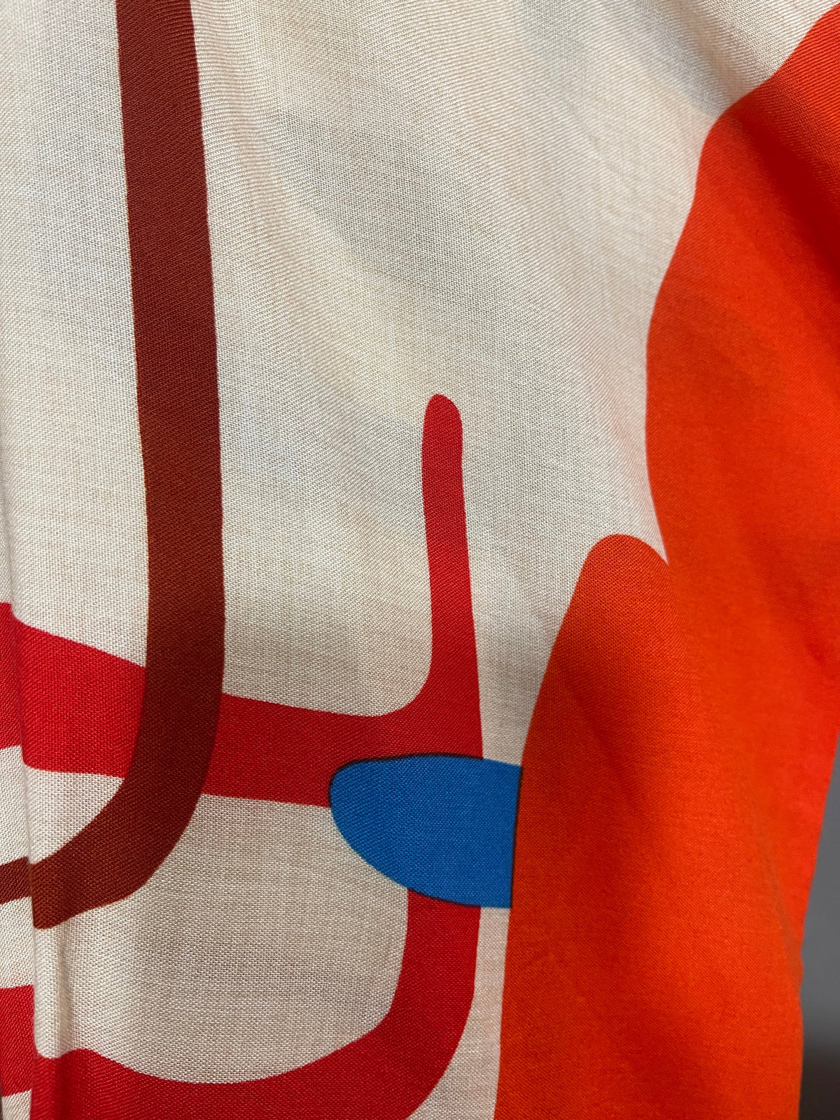 Original fabric close-up of the Abstract Print Tiered Dress, showing beige cloth and orange, red, brown and blue printed shapes.